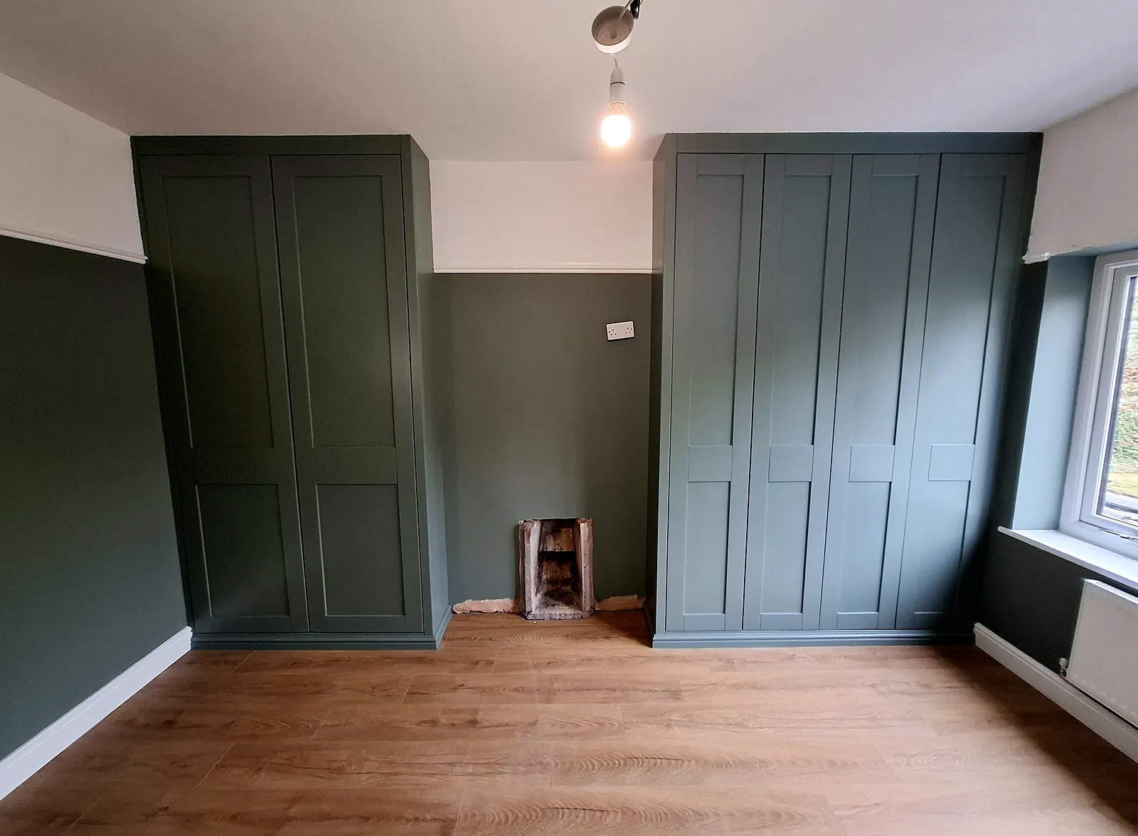 Pair of painted green shaker fitted wardrobes built into the alcoves either side of a chimney breast